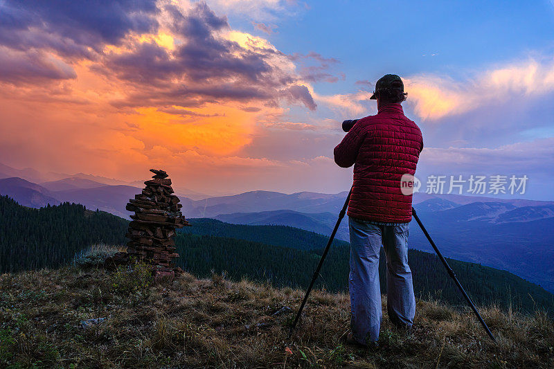 Photographer on Mountain Ridge Capturing Dramatic Sunset Landscape
